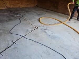 Cracked concrete floor in an empty room; cables and a large orange hose are spread across, held by a person in work boots.
