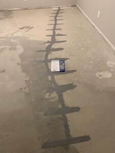 Crack Stitch carbon fiber crack repair installed on a concrete floor in a San Diego Ranch-style home. The image shows a repaired crack reinforced with Crack Stitch stitches and filled with epoxy, alongside an instruction sheet detailing the installation process.