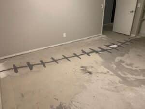 Crack Stitch carbon fiber crack repair installed on a concrete floor in a San Diego Ranch-style home. The image shows a repaired crack reinforced with Crack Stitch stitches and filled with epoxy.