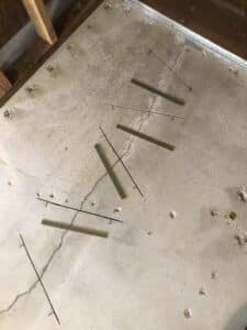 Close-up view of the Crack Stitch repair in progress, with carbon fiber staples embedded and bonded into the concrete, and a worker applying finishing touches in the background.