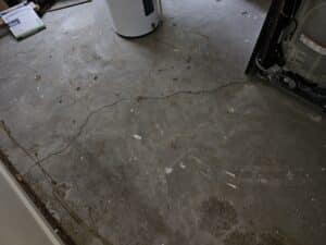 A cracked concrete basement floor with a dirty surface and a water heater positioned in the center.