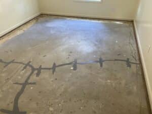 An unfinished concrete floor with marked lines of crack stitches inserted and patches, showing signs of wear and dirt in an unfinished room.